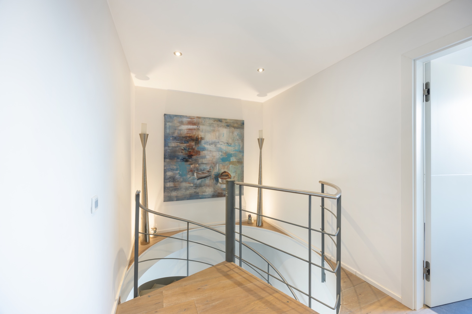 Heller Flur mit runder Treppe, abstraktem Gemälde und zwei Stehlampen an der Wand.