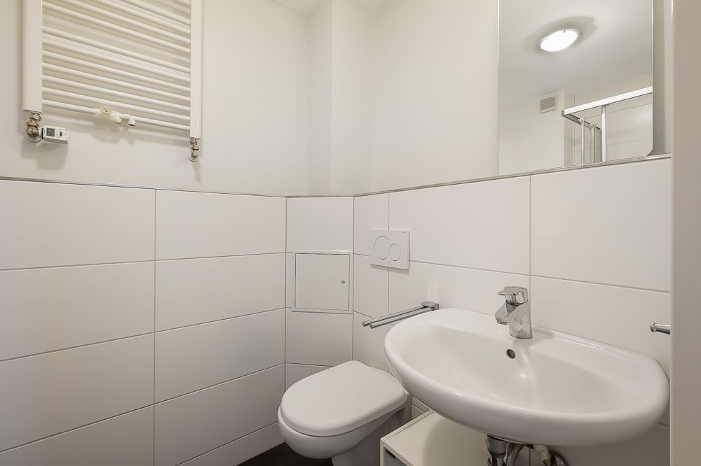 Helles Badezimmer mit Wandtoilette, Waschbecken und Spiegel.