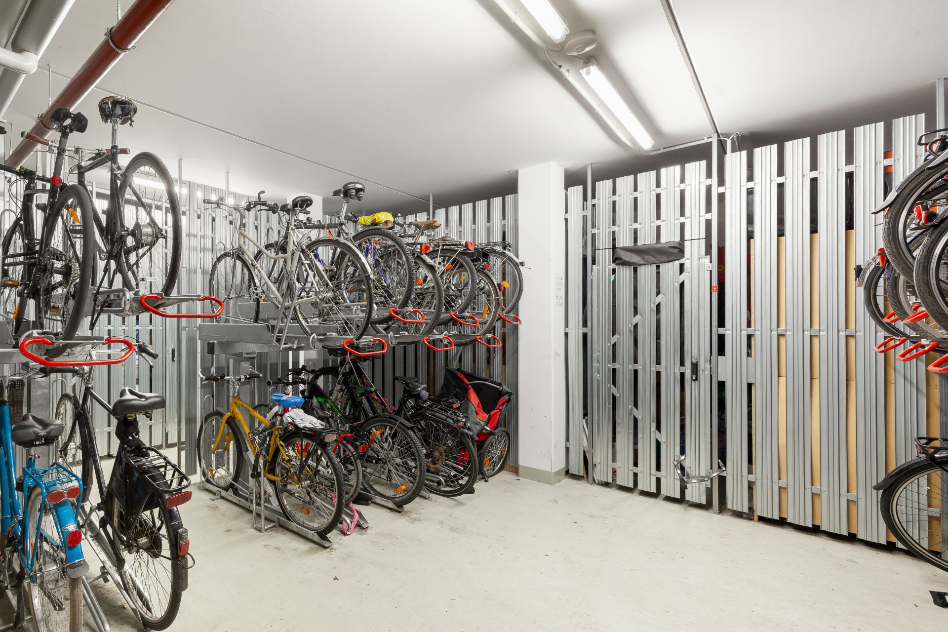 Heller Fahrradkeller mit gestapelten Fahrrädern und Metallgitterwänden.