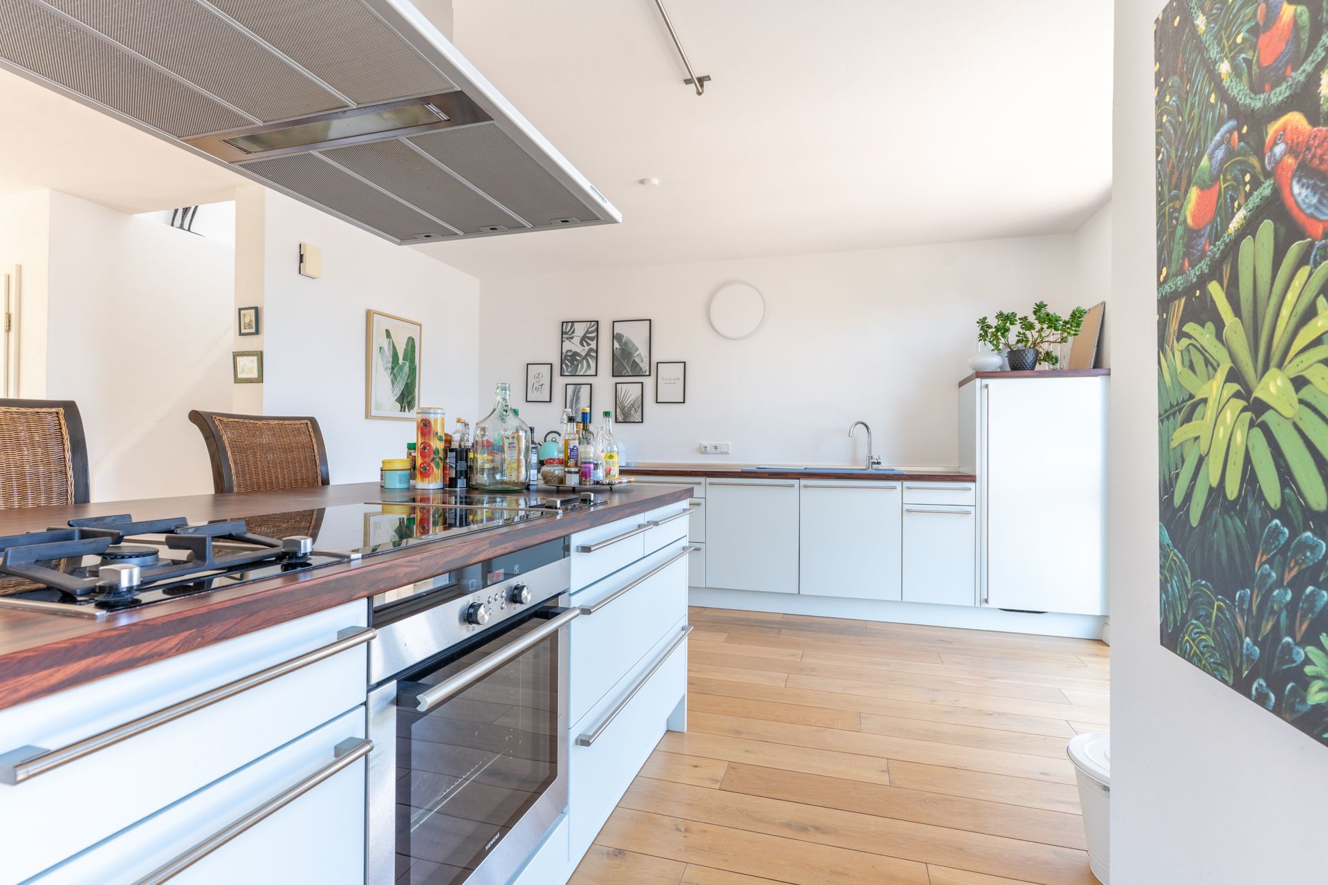 Helle, moderne Küche mit Holzfußboden, Kochinsel und weißen Schränken.