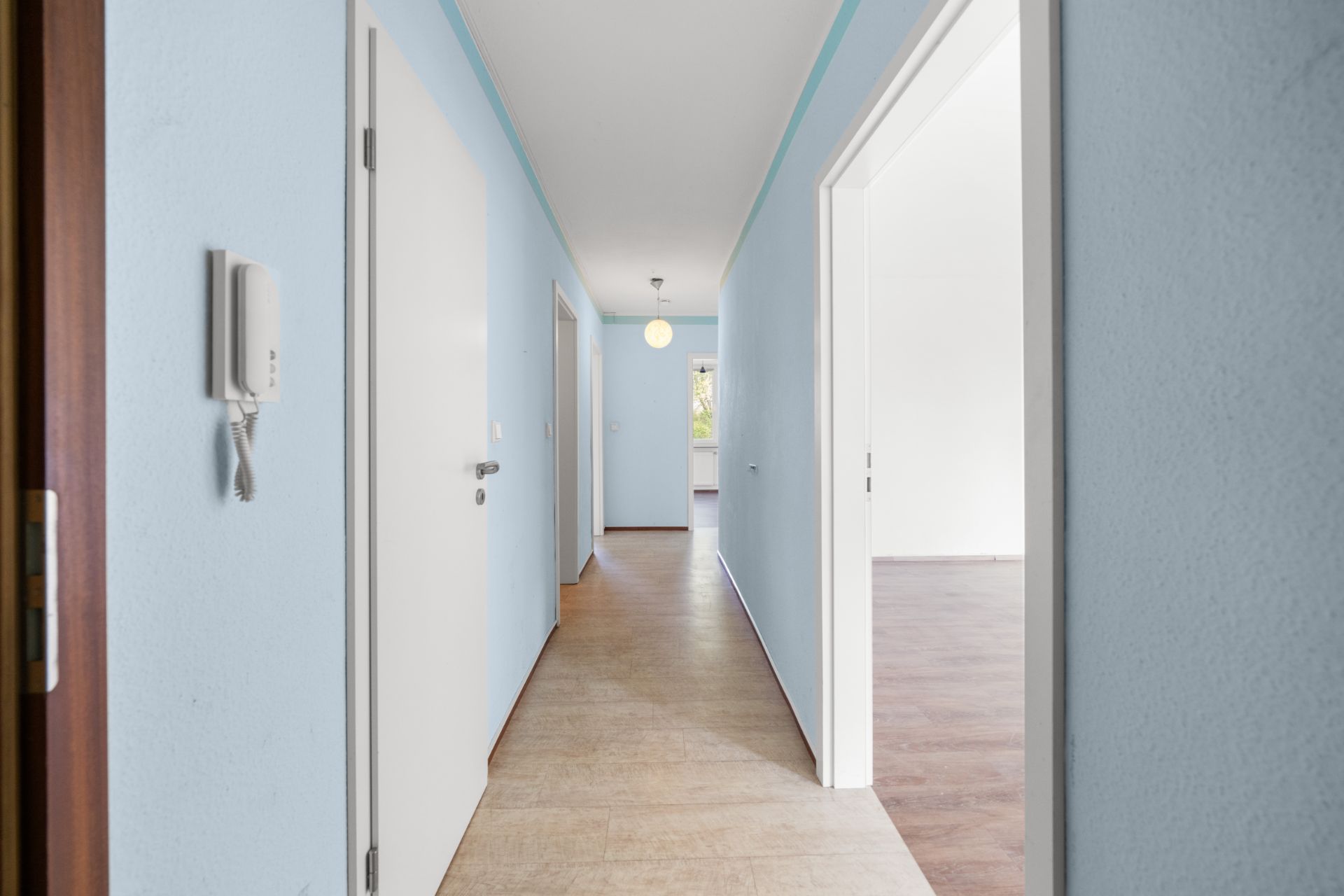 Heller Flur mit blauen Wänden, mehreren Türen und Blick auf ein Fenster am Ende.