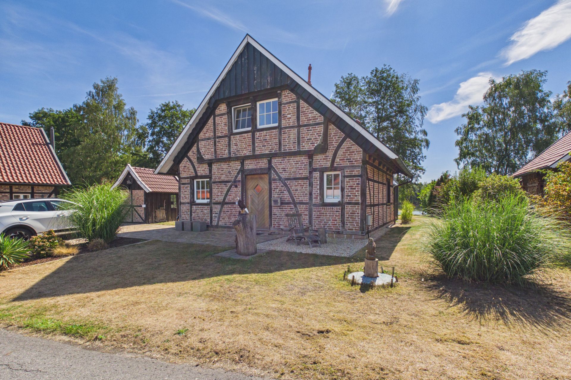 Fachwerkhaus mit Satteldach, Vorgarten und umgebender Begrünung bei Sonnenschein.