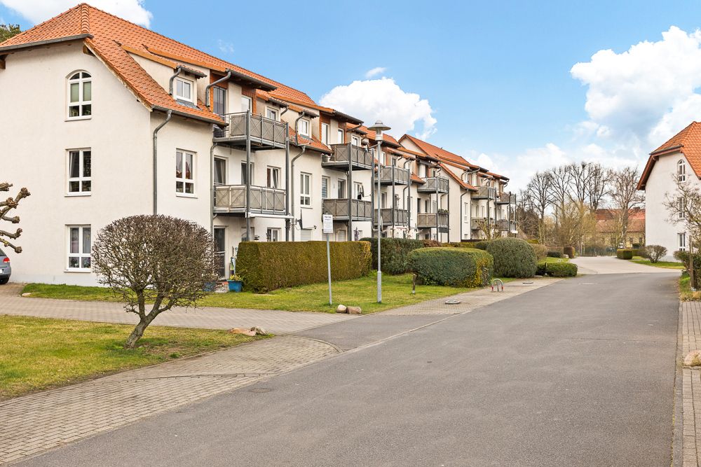 Mehrfamilienhaus mit Balkonen, Vorgarten und Gehweg bei sonnigem Wetter.