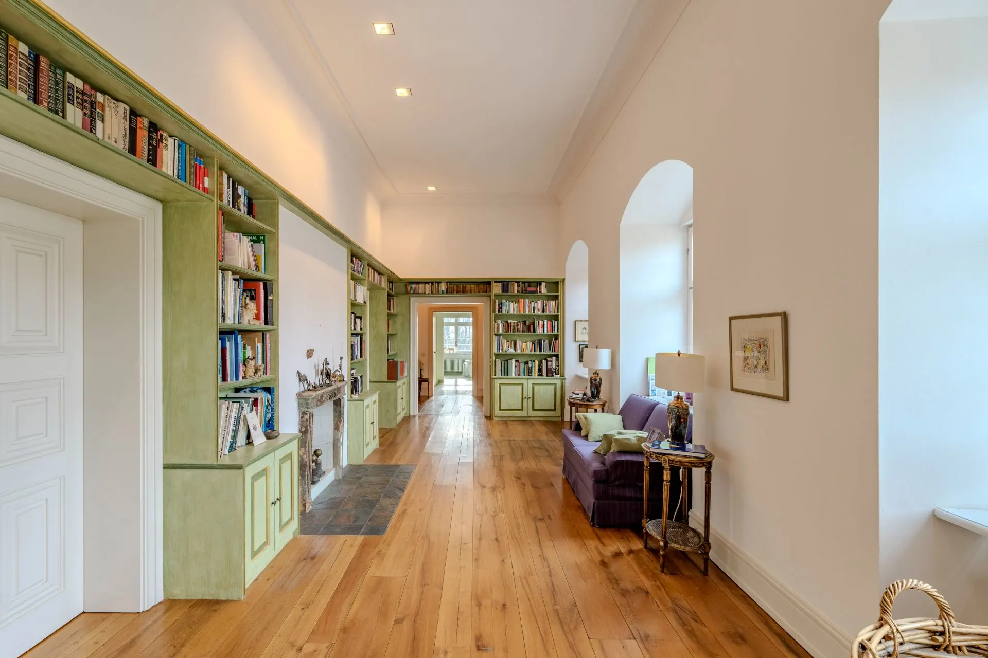 Heller Flur mit Holzboden, Bücherregalen, Sofa und großen Fenstern.