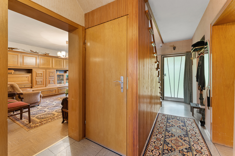 Flur mit Holzvertäfelung, Teppichläufer und Blick ins Wohnzimmer mit Holzschränken.