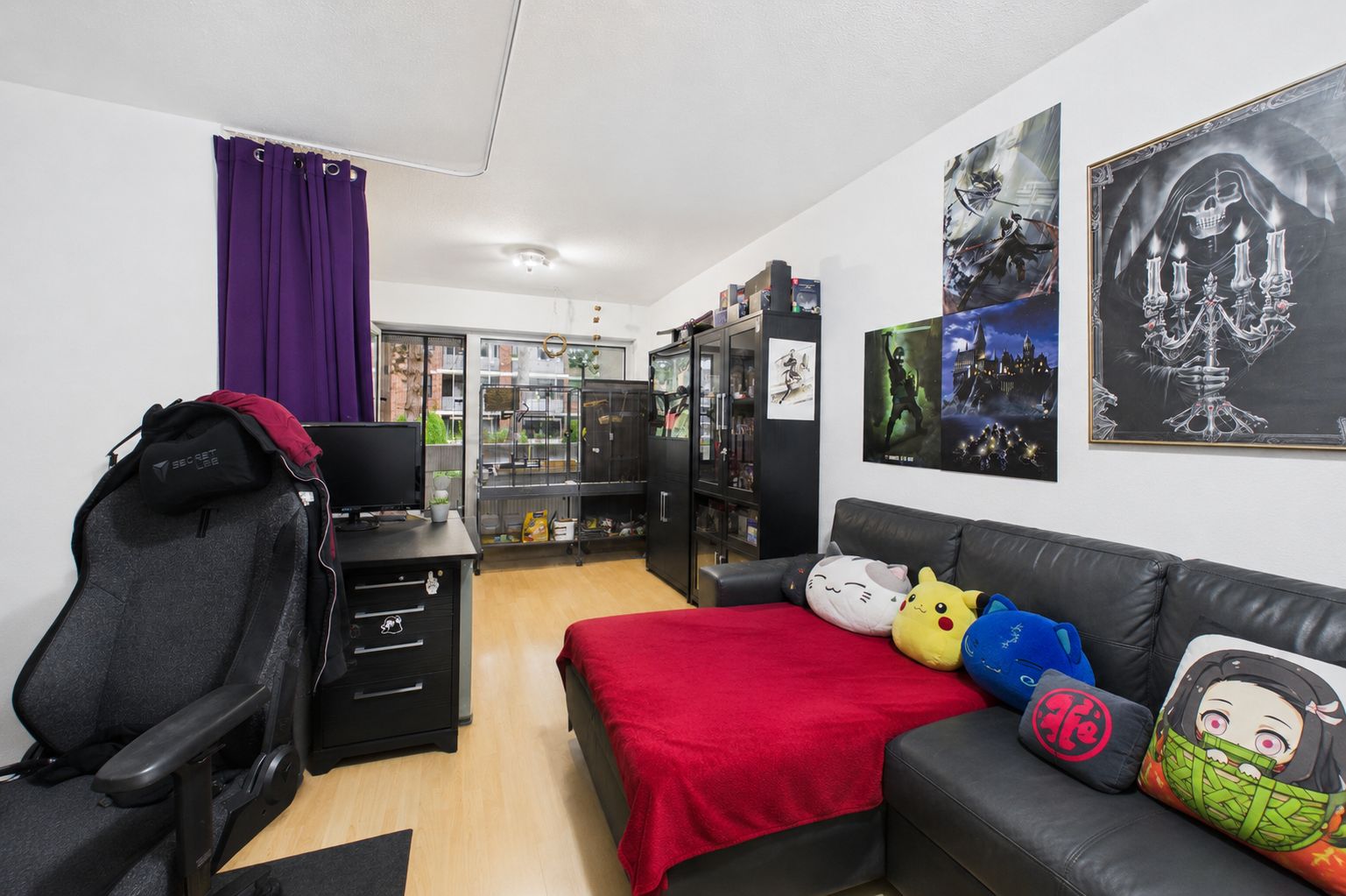 Wohnzimmer mit schwarzem Sofa, roter Decke, Schreibtisch, Vitrine und bunten Kissen.
