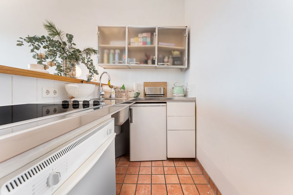 Moderne kleine Küche mit Herd, Spüle, Kühlschrank und Hängeschränken, terrakottafarbener Fliesenboden.