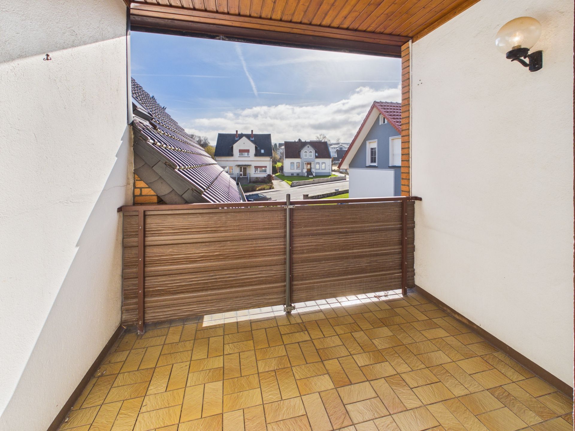 Überdachter Balkon mit Fliesenboden und Blick auf Nachbarhäuser bei Tageslicht.
