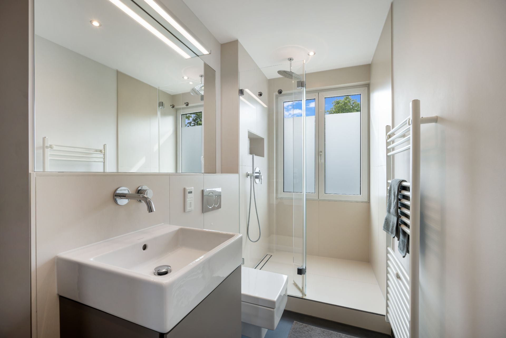 Modernes Badezimmer mit großem Spiegel, Dusche, Waschbecken, WC und Fenster.