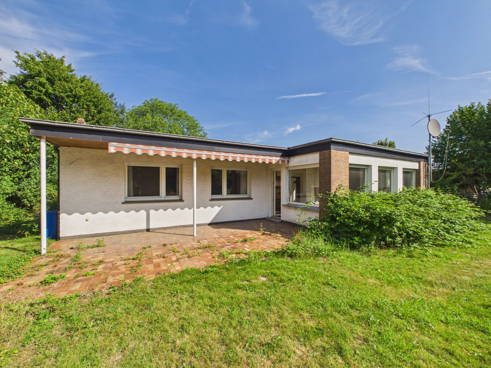 Einfamilienhaus mit Terrasse, Markise und Garten, umgeben von Bäumen.