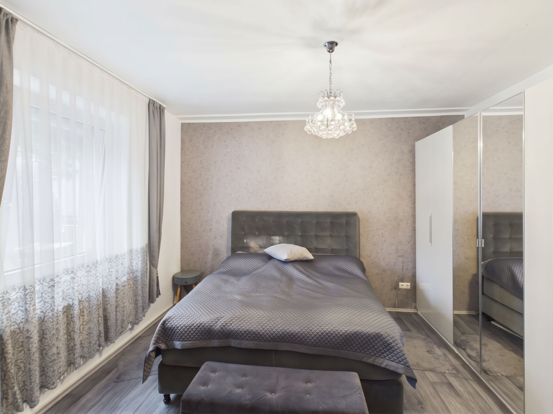 Schlafzimmer mit Doppelbett, Nachttisch, Kronleuchter und Kleiderschrank mit Spiegel.