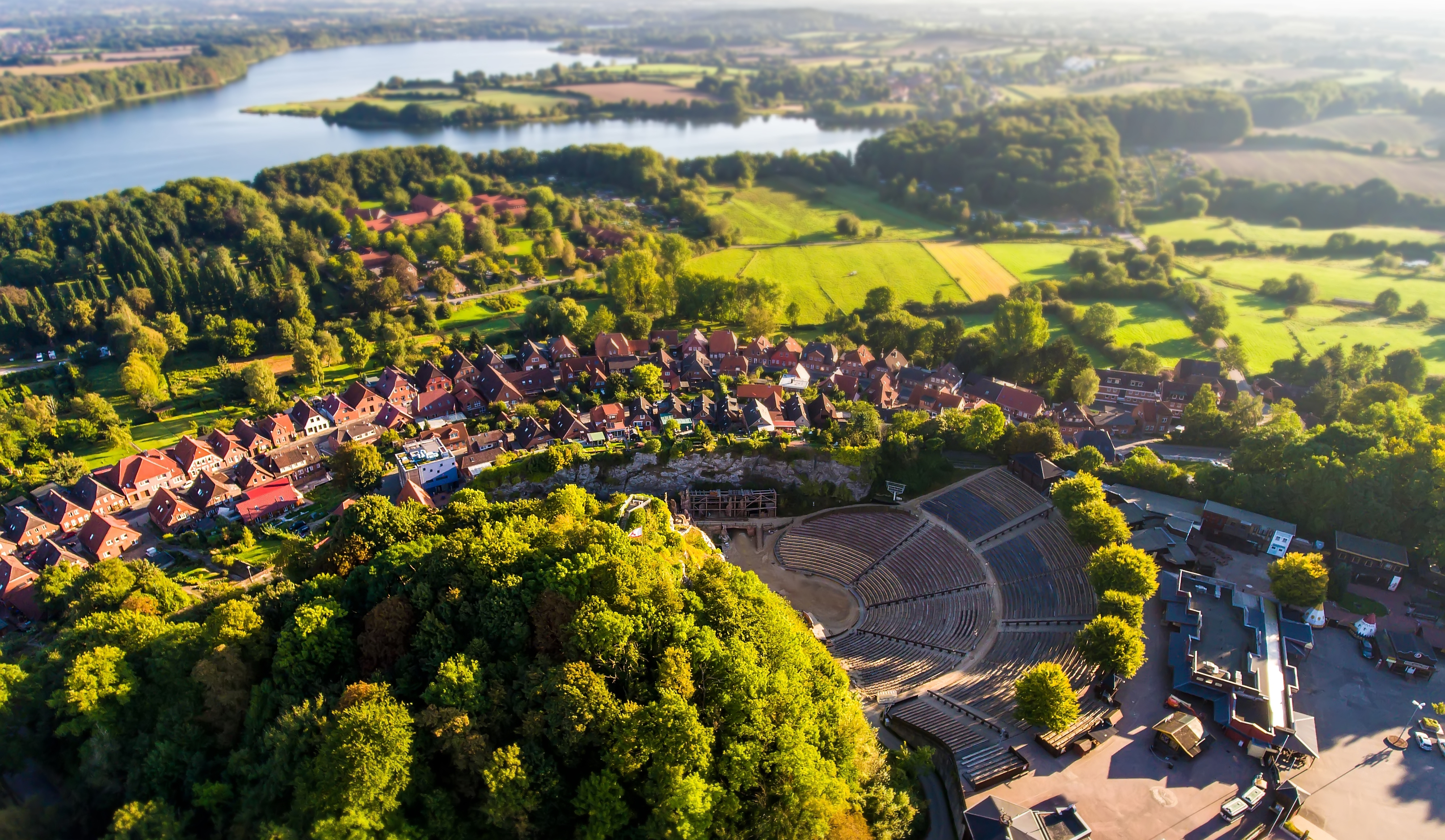 Luftaufnahme einer Küstenstadt mit Strand, Meer, Häusern und Bäumen bei sonnigem Wetter.