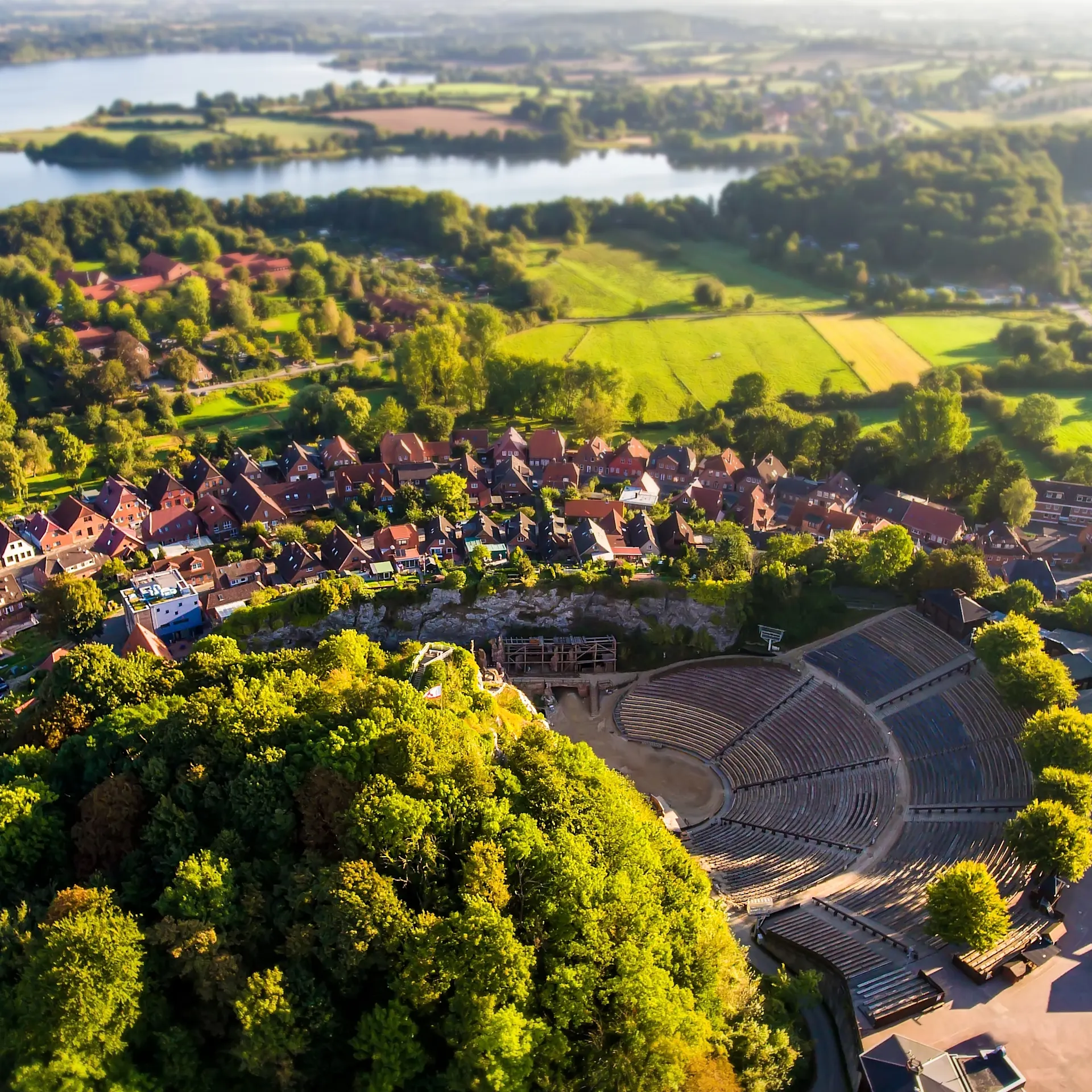 Luftaufnahme einer Küstenstadt mit Strand, Meer, Häusern und Bäumen bei sonnigem Wetter.