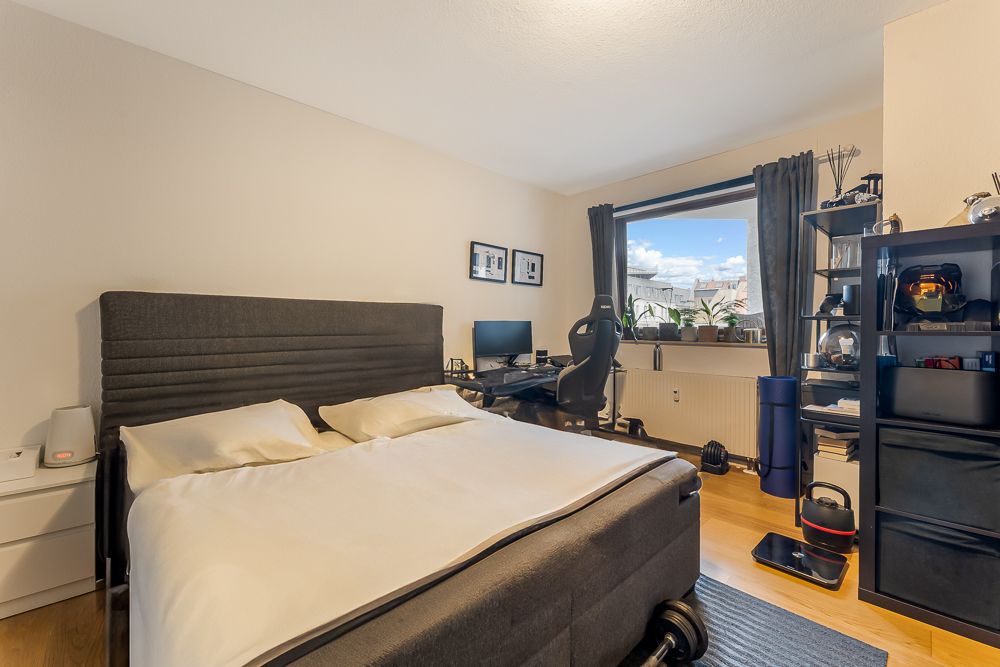 Schlafzimmer mit Doppelbett, Schreibtisch, Computer, Regal und Fenster mit Blick nach draußen.
