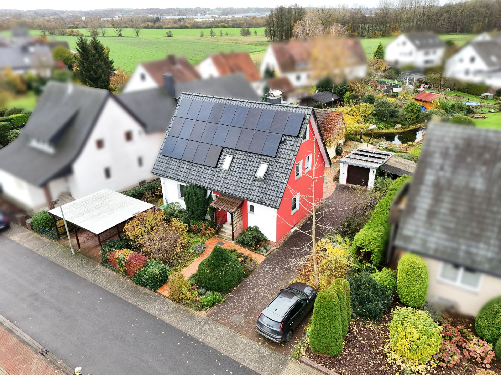 Rotes Einfamilienhaus mit Solaranlage auf dem Dach, Garten und Einfahrt mit Auto.