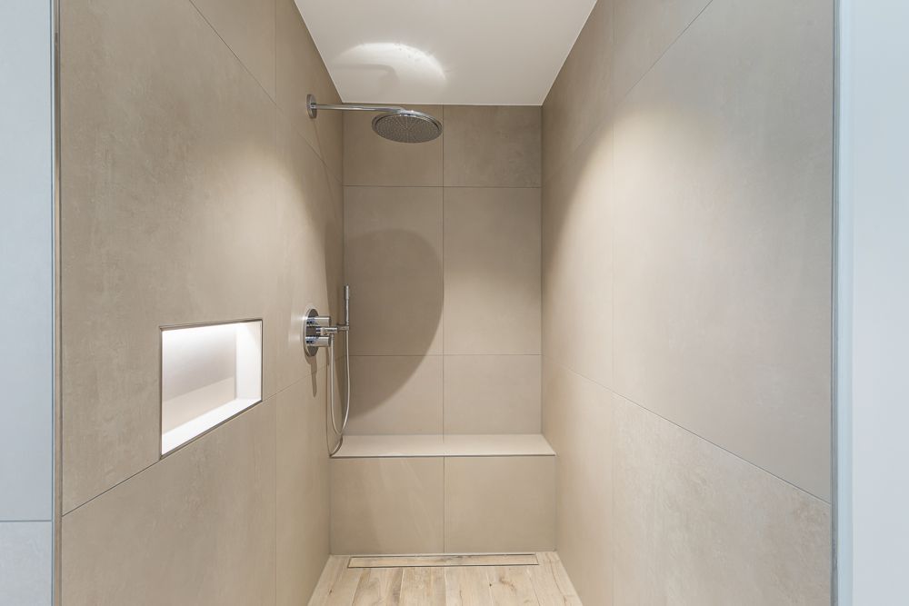 Moderne begehbare Dusche mit Sitzbank, Regendusche und beleuchtetem Wandfach.