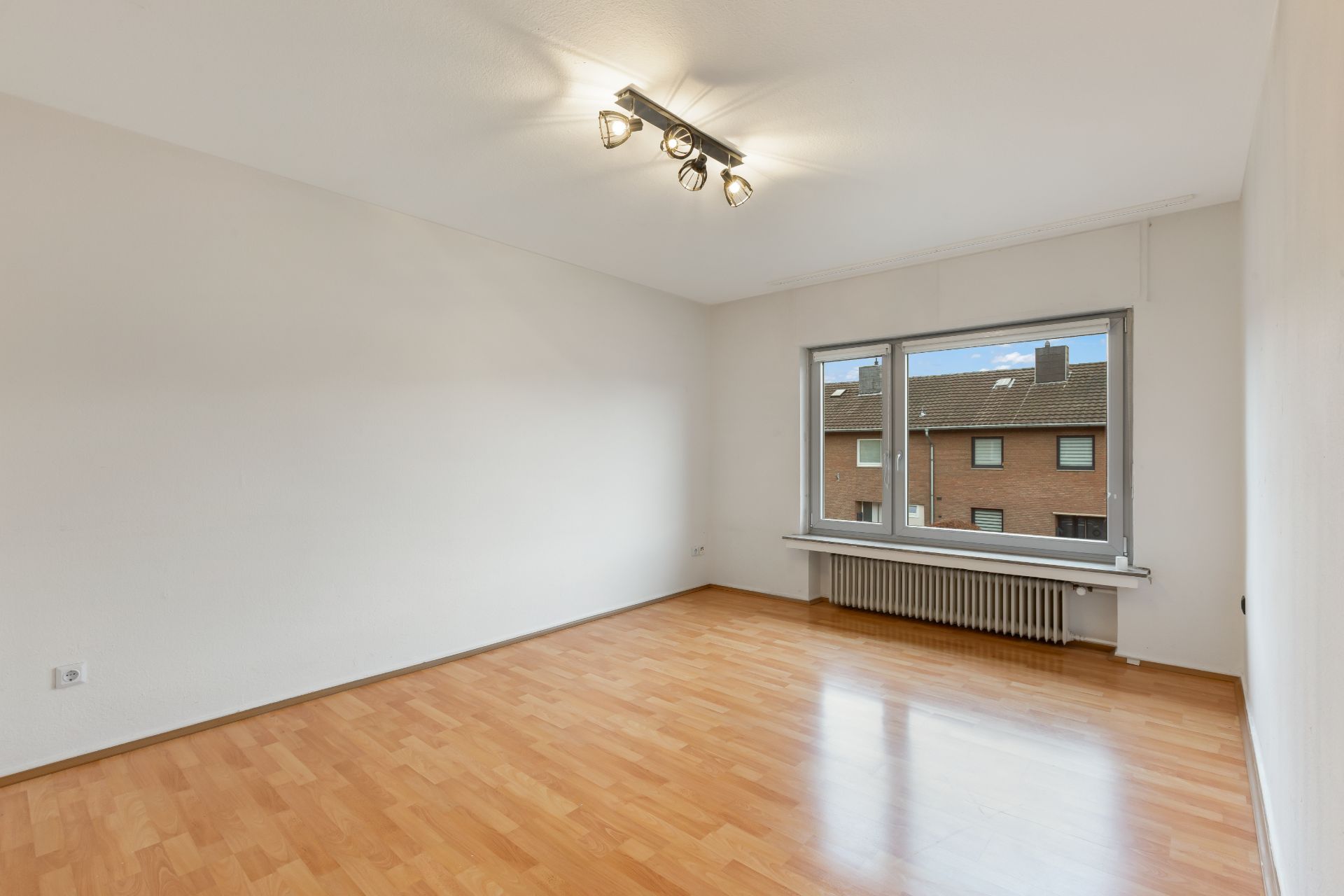 Leerer Raum mit Holzfußboden, weißer Wand, großem Fenster und Deckenleuchte.