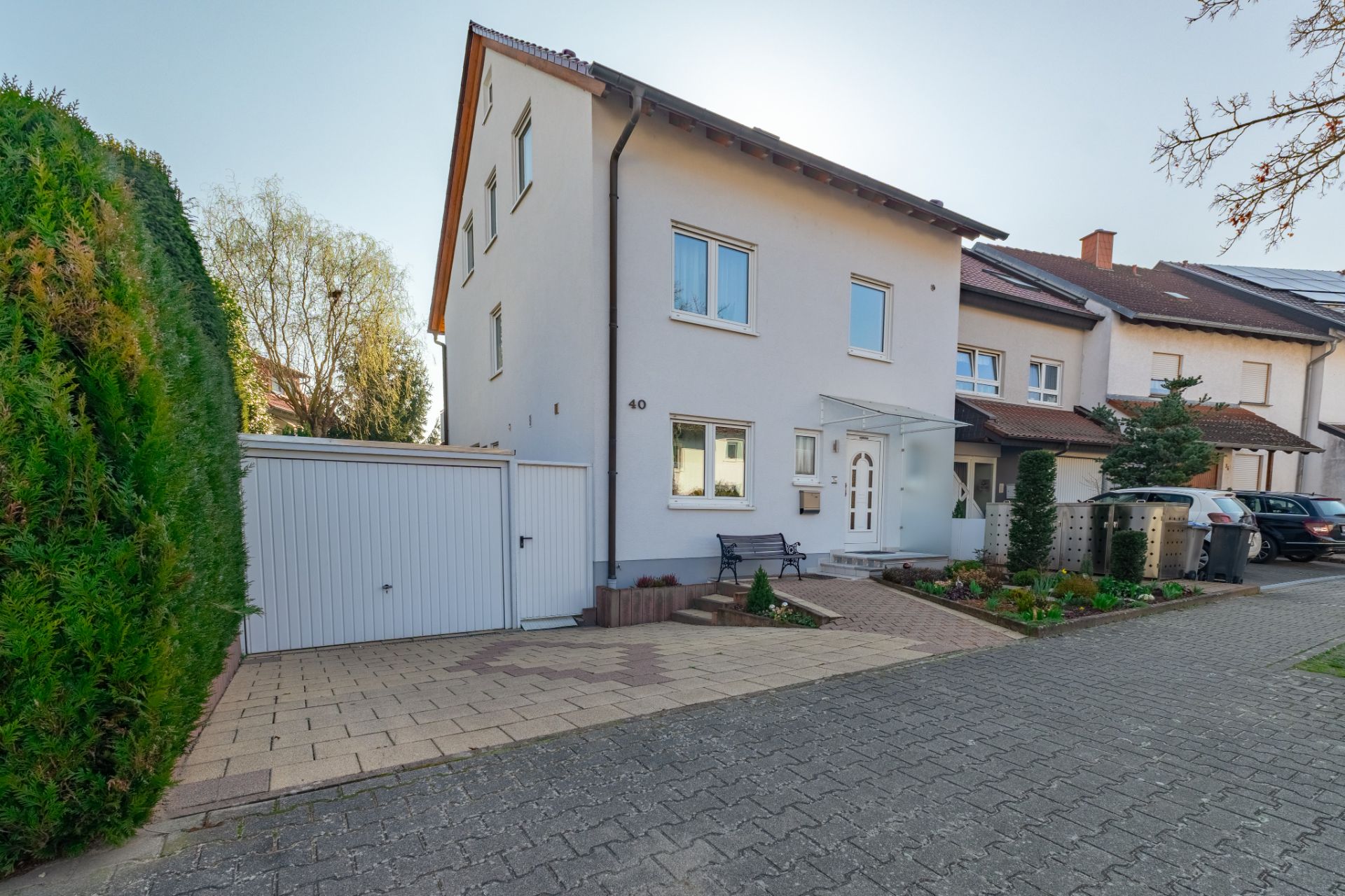 Zweistöckiges weißes Wohnhaus mit Garage, Vorgarten und gepflasterter Einfahrt.