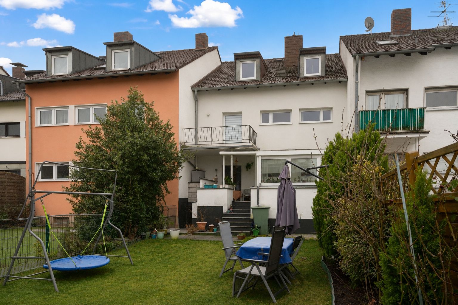 Rückseite eines Wohnhauses mit Garten, Schaukel, Tisch und Stühlen auf Grasfläche.