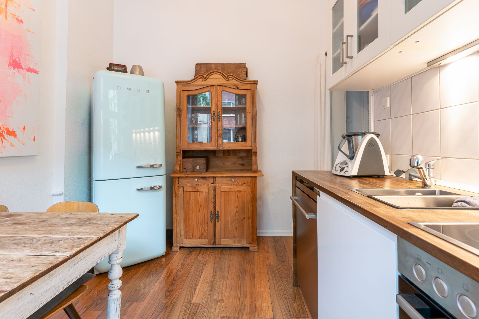 Küche mit blauem Kühlschrank, Holzschrank, Spüle und Holztisch auf Holzfußboden.