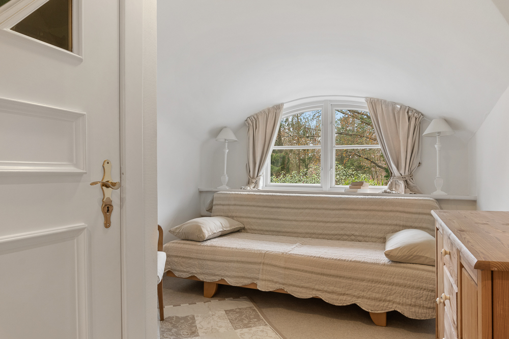 Kleines Zimmer mit Sofa, zwei Kissen, bogenförmigem Fenster und hellen Vorhängen.