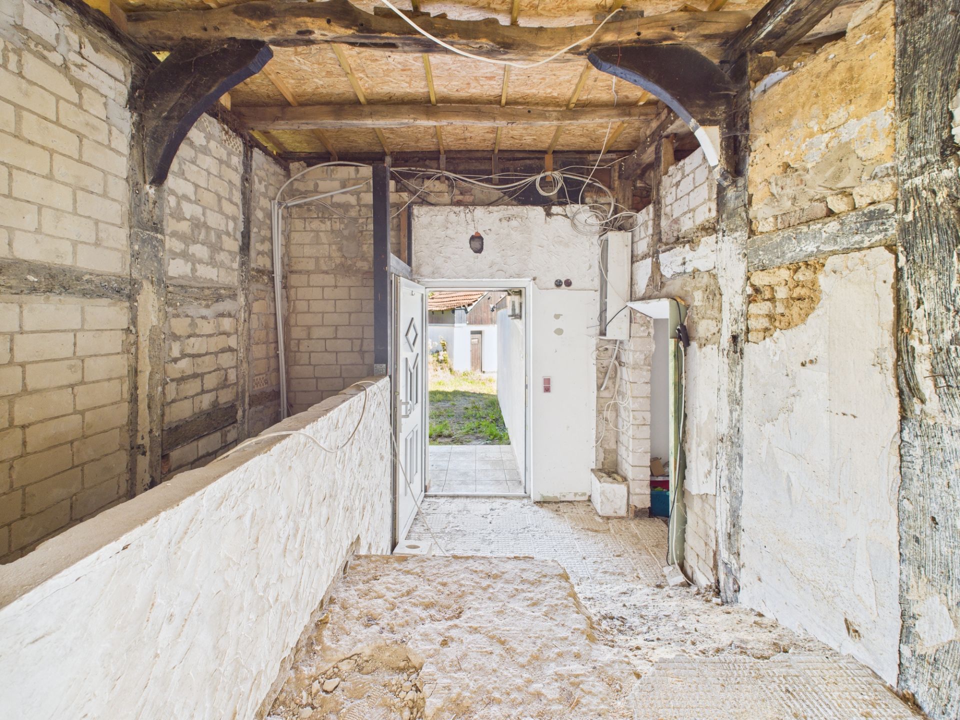 Renovierungsbedürftiger Flur mit offenen Wänden und sichtbaren Holzbalken.