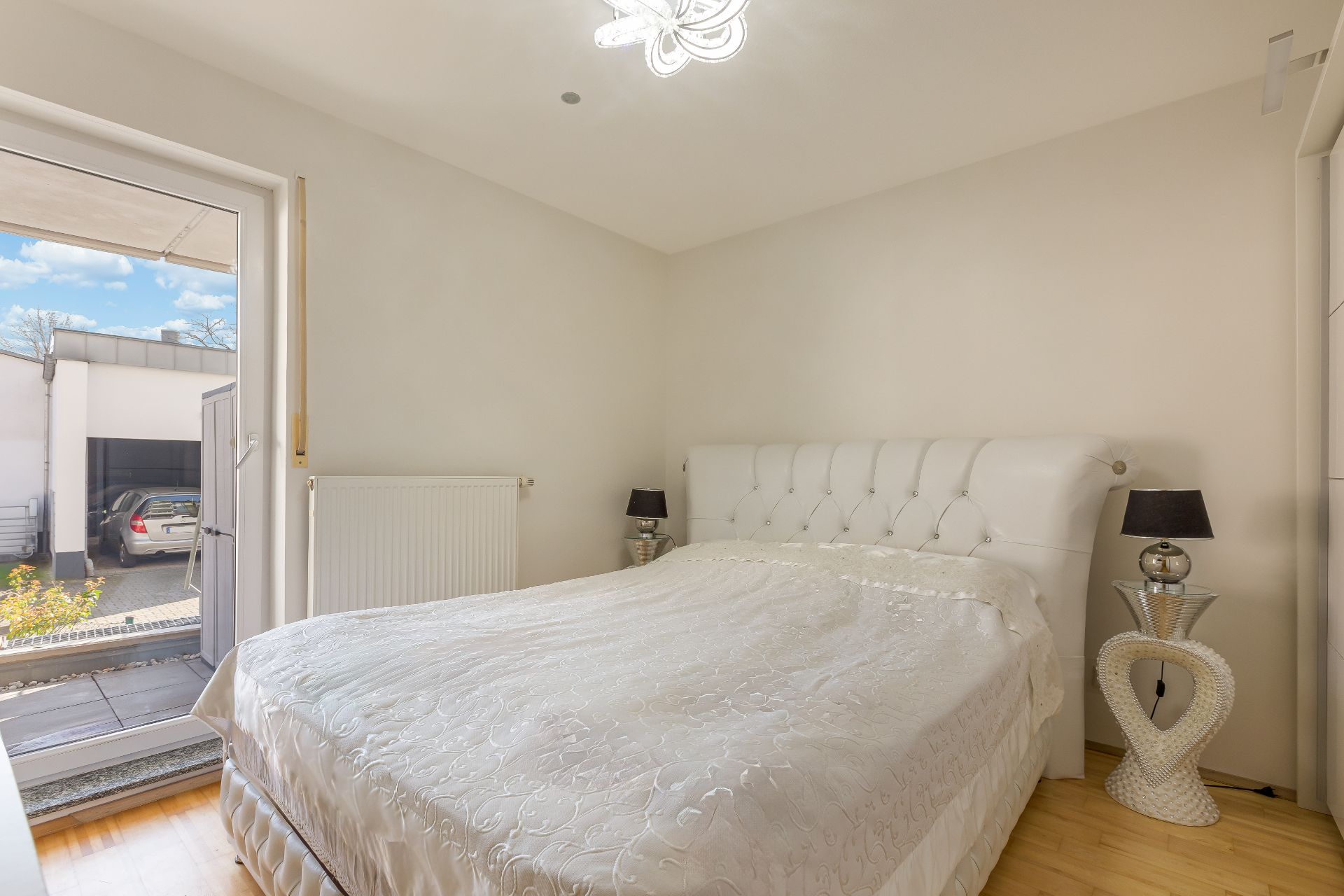 Helles Schlafzimmer mit weißem Bett, zwei Nachttischen und Zugang zur Terrasse.