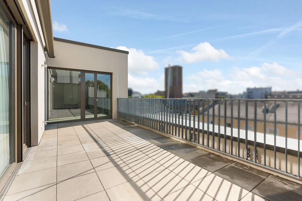 Große Dachterrasse mit Fliesenboden, Geländer und Glas-Schiebetüren, Blick auf die Stadt.