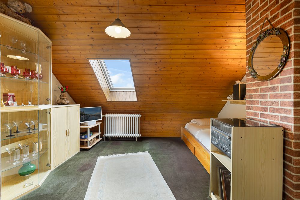 Gemütliches Dachzimmer mit Holzdecke, Glasvitrine, Teppich, Sofa und Dachfenster.