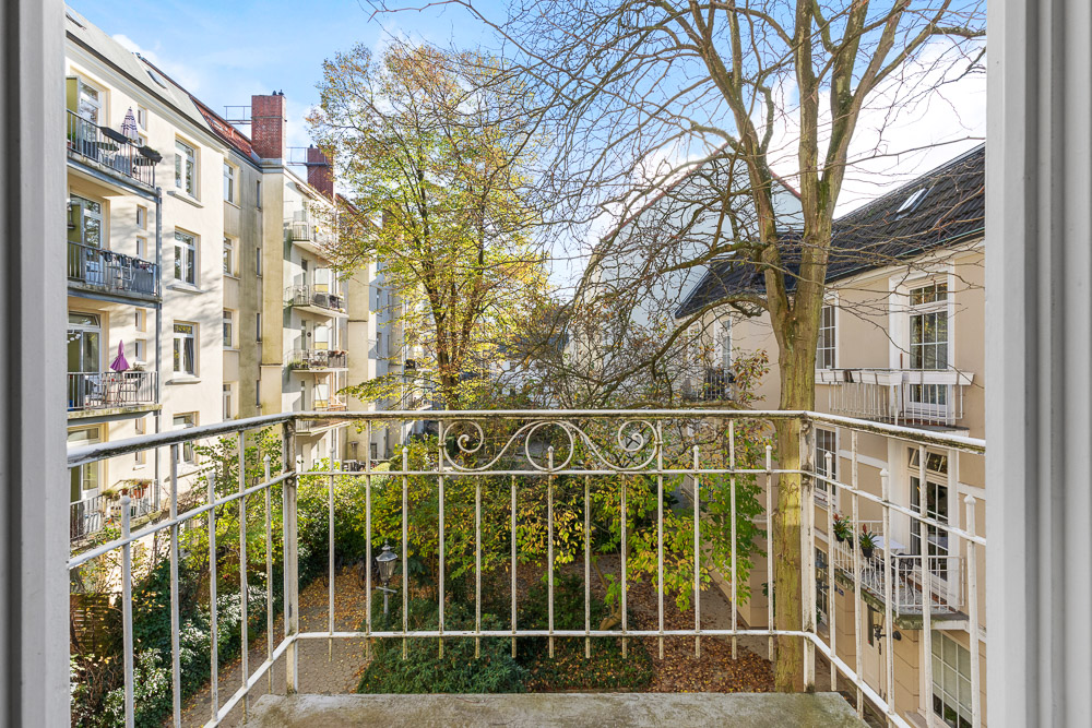 Blick von einem Balkon auf einen begrünten Innenhof und umliegende Wohnhäuser.