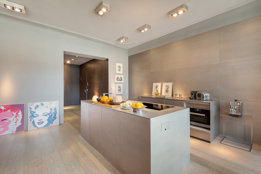 Moderne Küche mit Kochinsel, Kunstwerken und Küchengeräten auf hellen Holzboden.