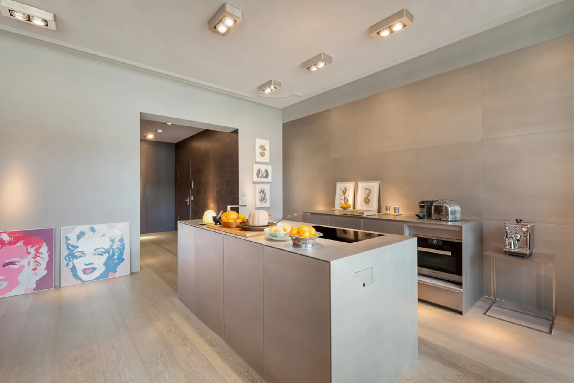 Moderne Küche mit Kochinsel, Kunstwerken und Küchengeräten auf hellen Holzboden.