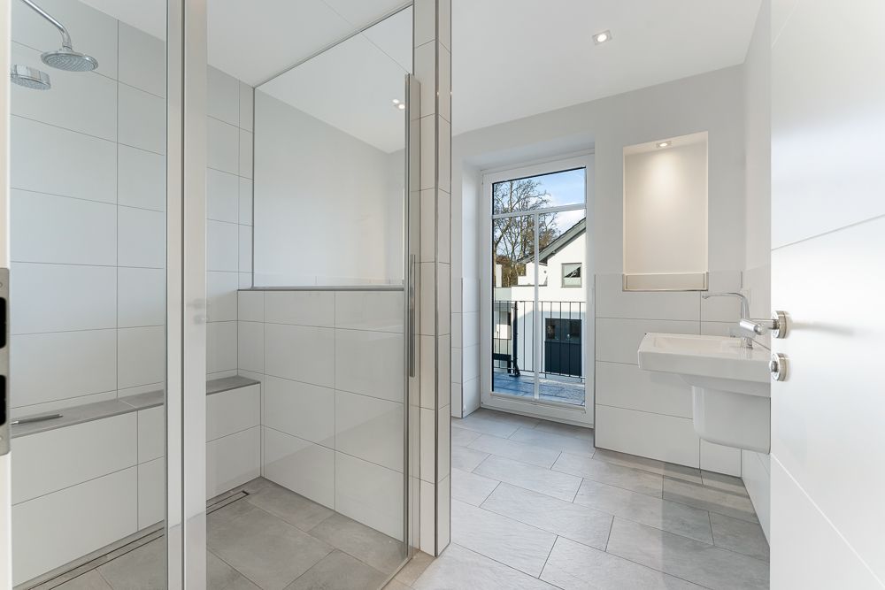 Modernes, helles Badezimmer mit Dusche, Waschbecken und Fenster mit Blick nach draußen.