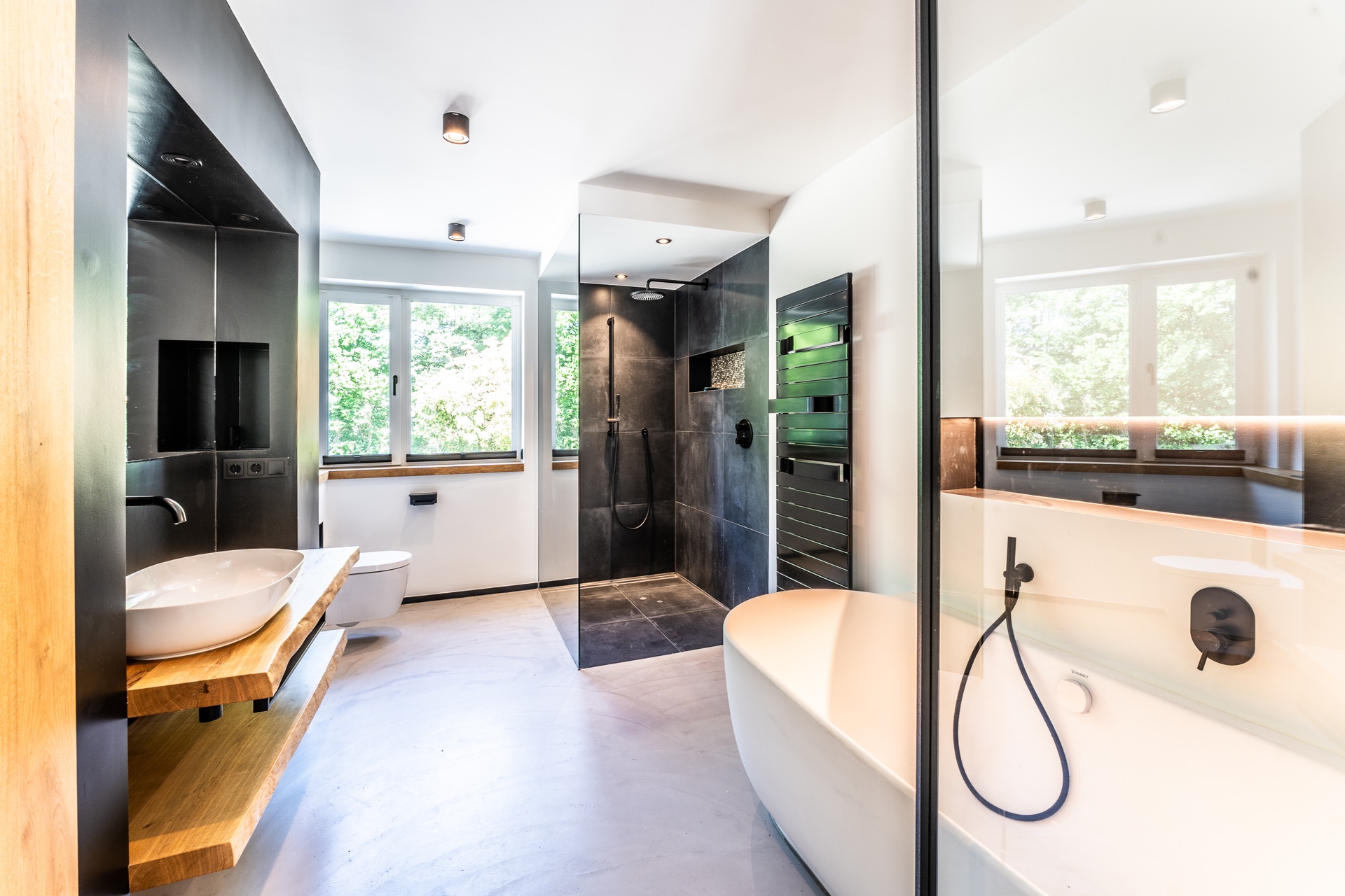 Modernes Badezimmer mit freistehender Badewanne, Dusche, Waschbecken und großen Fenstern.