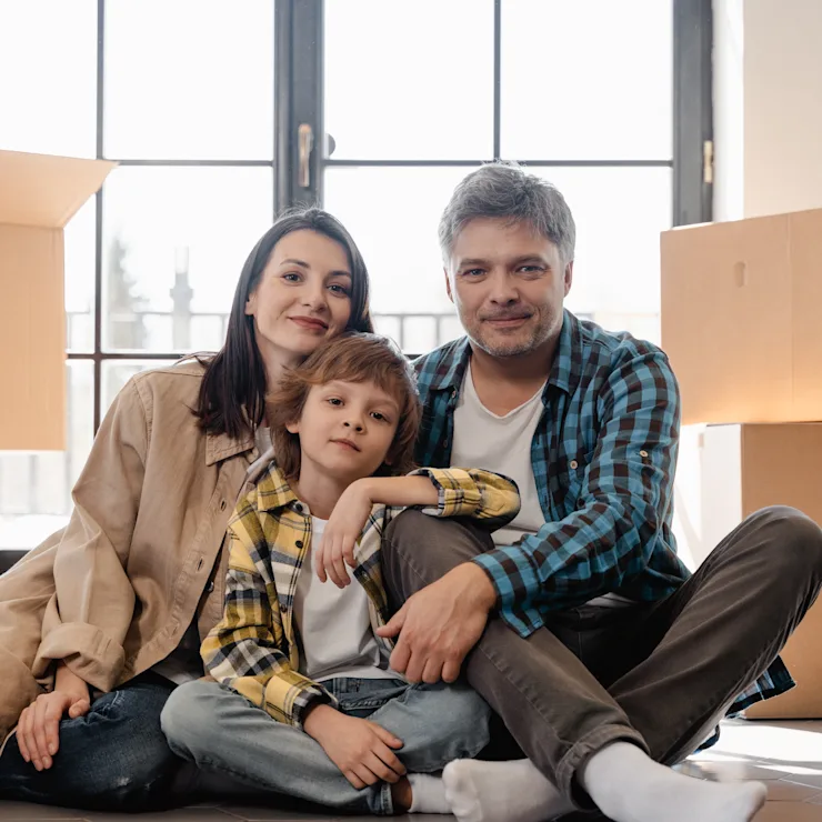 Una familia sentada en el suelo frente a grandes cajas de mudanza en una habitación luminosa.