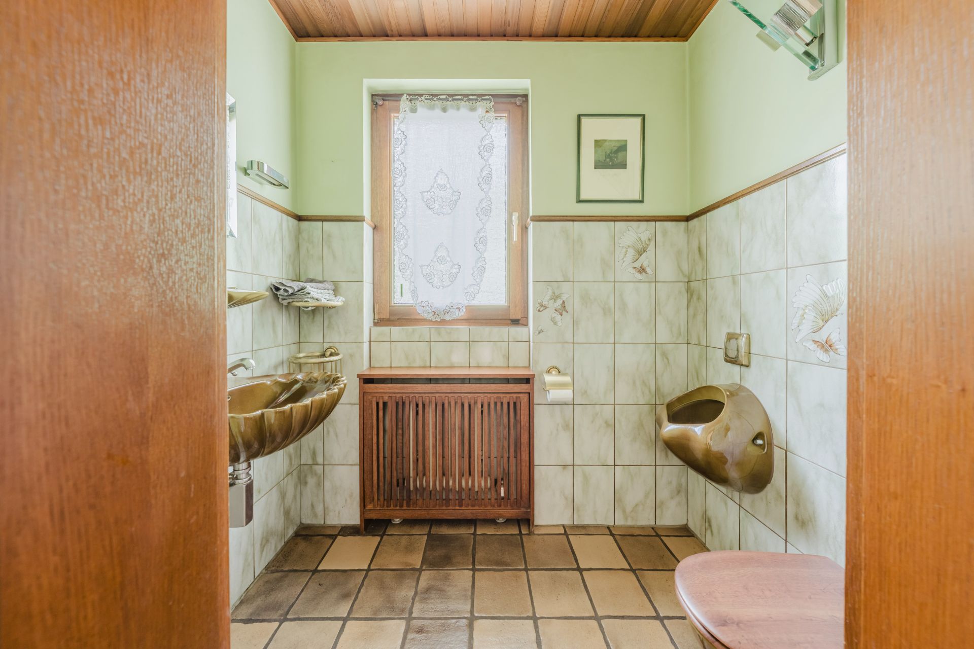 Badezimmer mit braunem Waschbecken, Toilette, Fenster und hellen Fliesen.