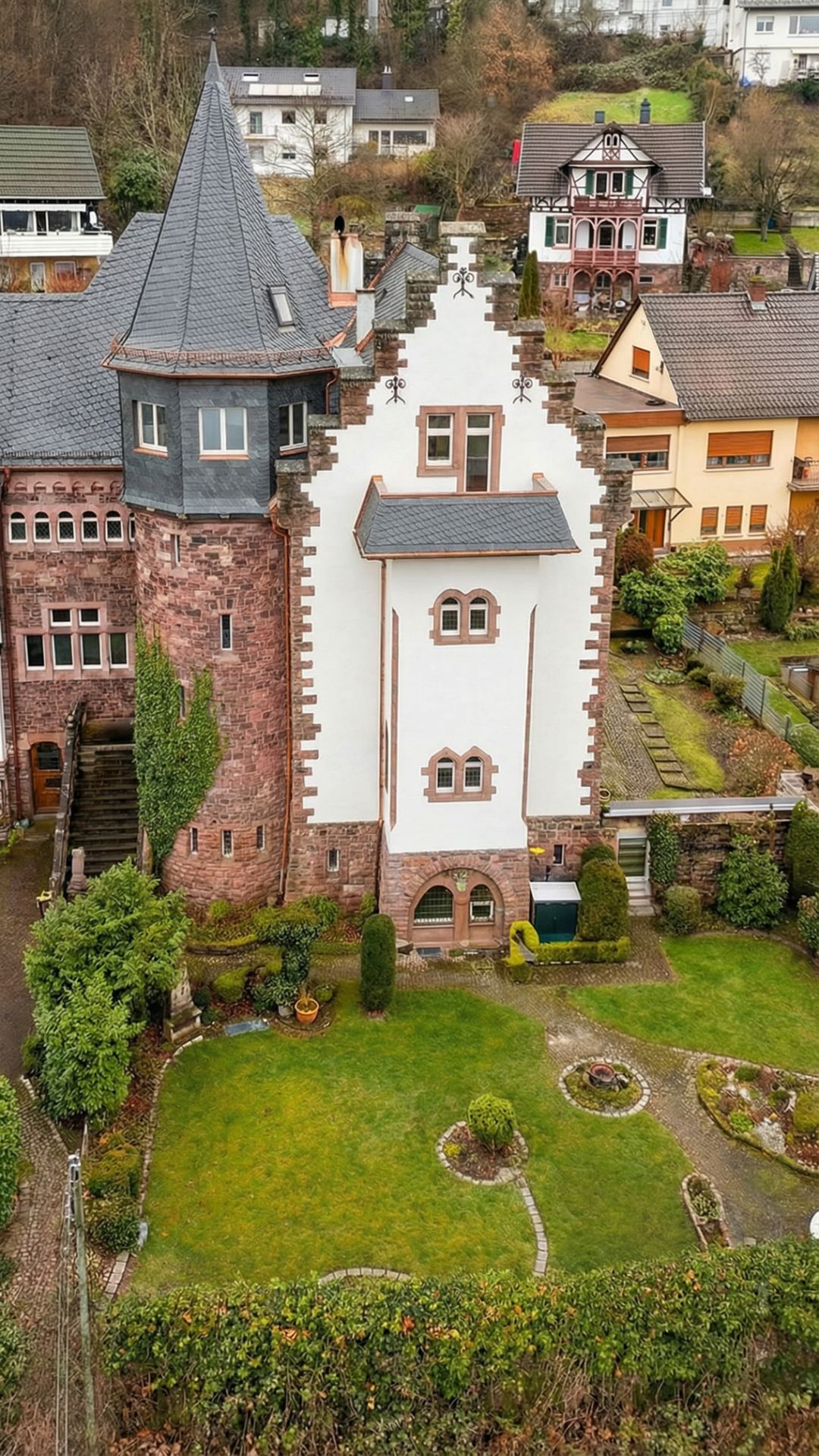 Großes Wohnhaus mit weißer Fassade, Turm und Garten, umgeben von weiteren Wohnhäusern.