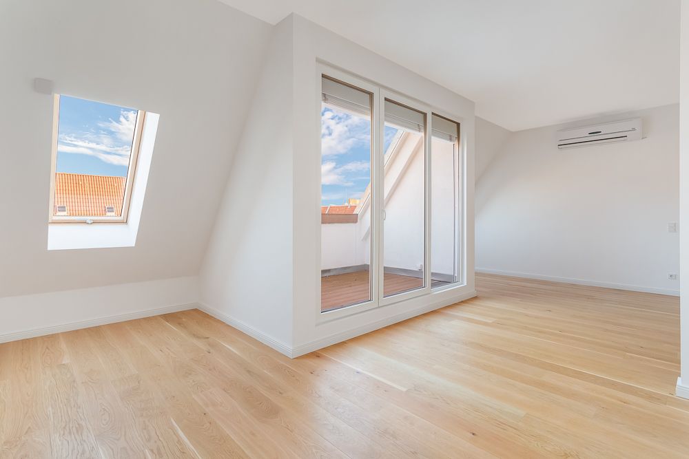 Helles Zimmer mit Parkettboden, Dachfenster, Glastür zum Balkon und Klimaanlage an der Wand.