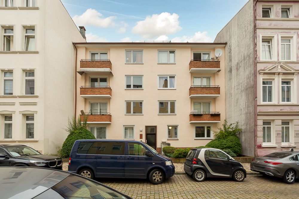 Mehrfamilienhaus mit vier Etagen, Balkonen und geparkten Autos davor.