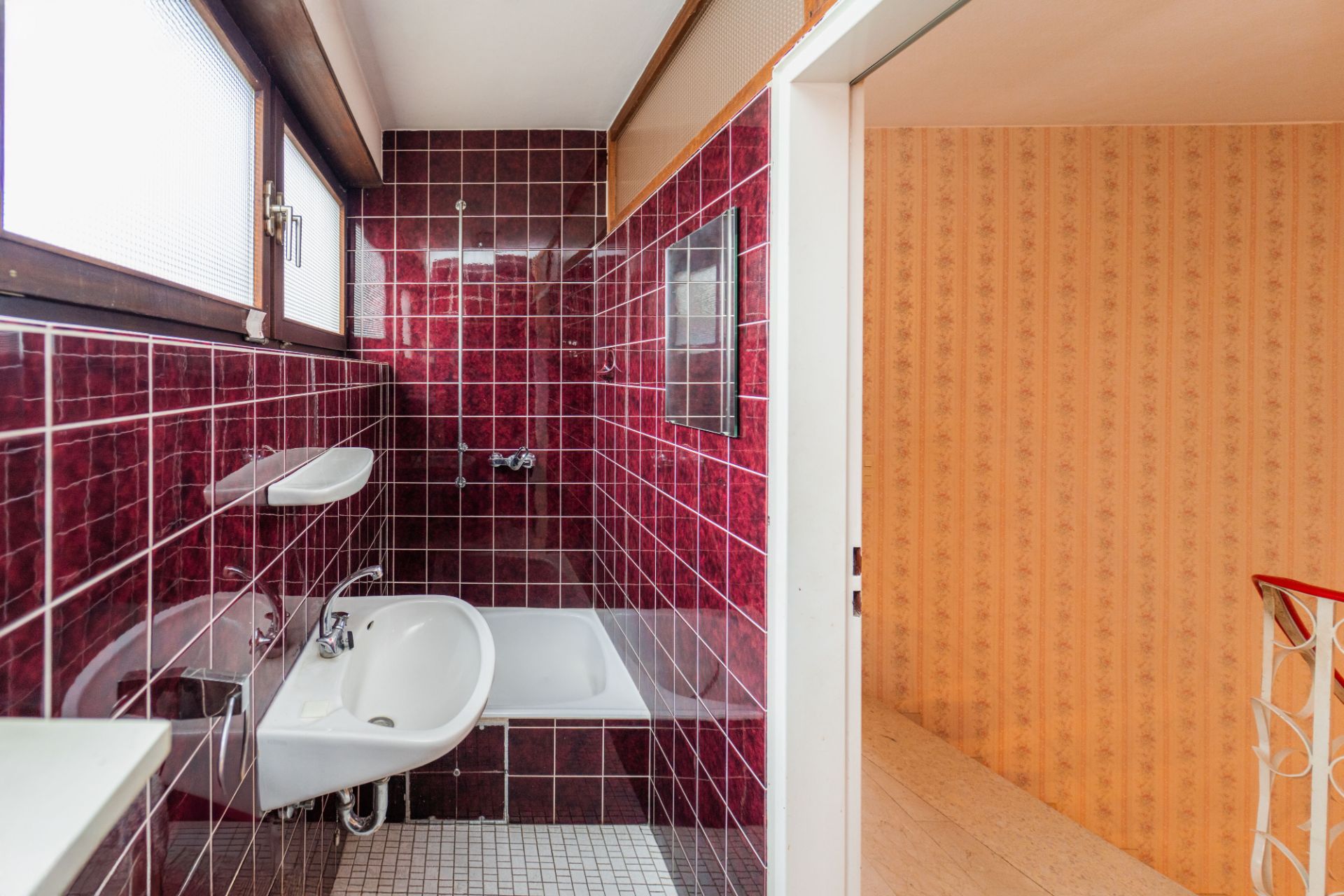 Kleines Bad mit roten Fliesen, Badewanne, Waschbecken und Fenster.