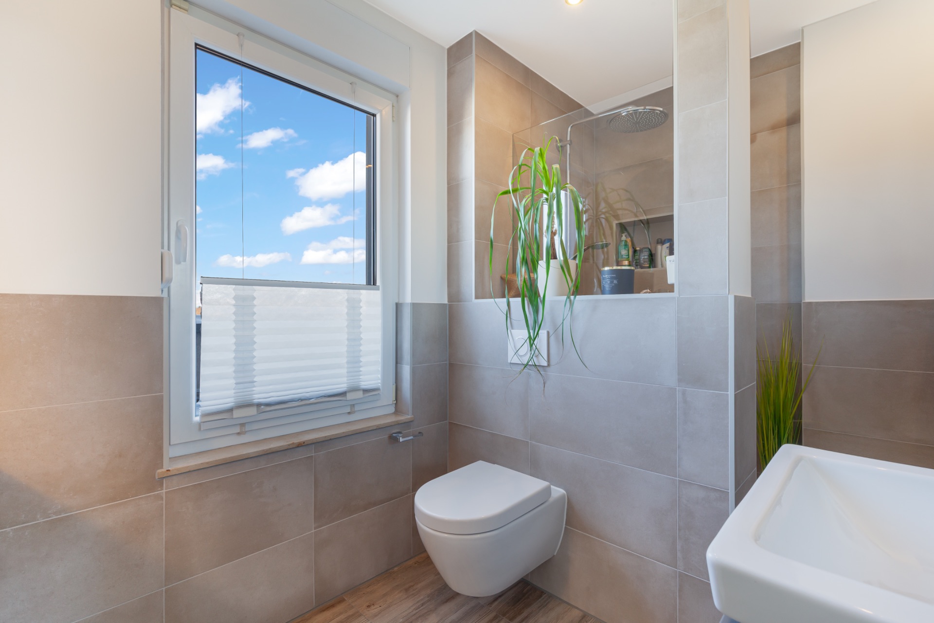 Modernes Badezimmer mit Fenster, Wand-WC, Waschbecken und grünen Pflanzen.