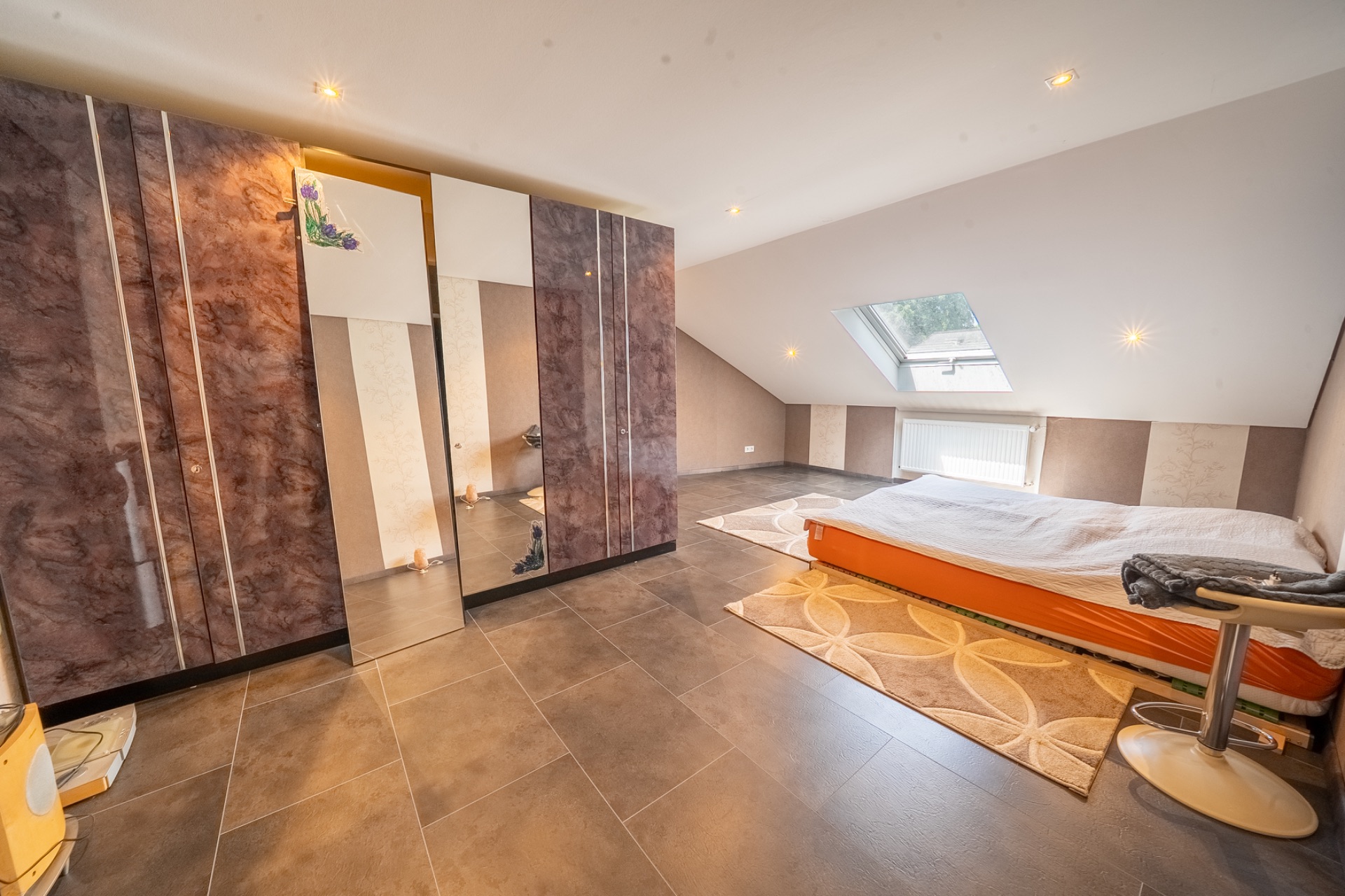 Schlafzimmer mit großem Kleiderschrank, niedrigem Bett und Dachfenster.