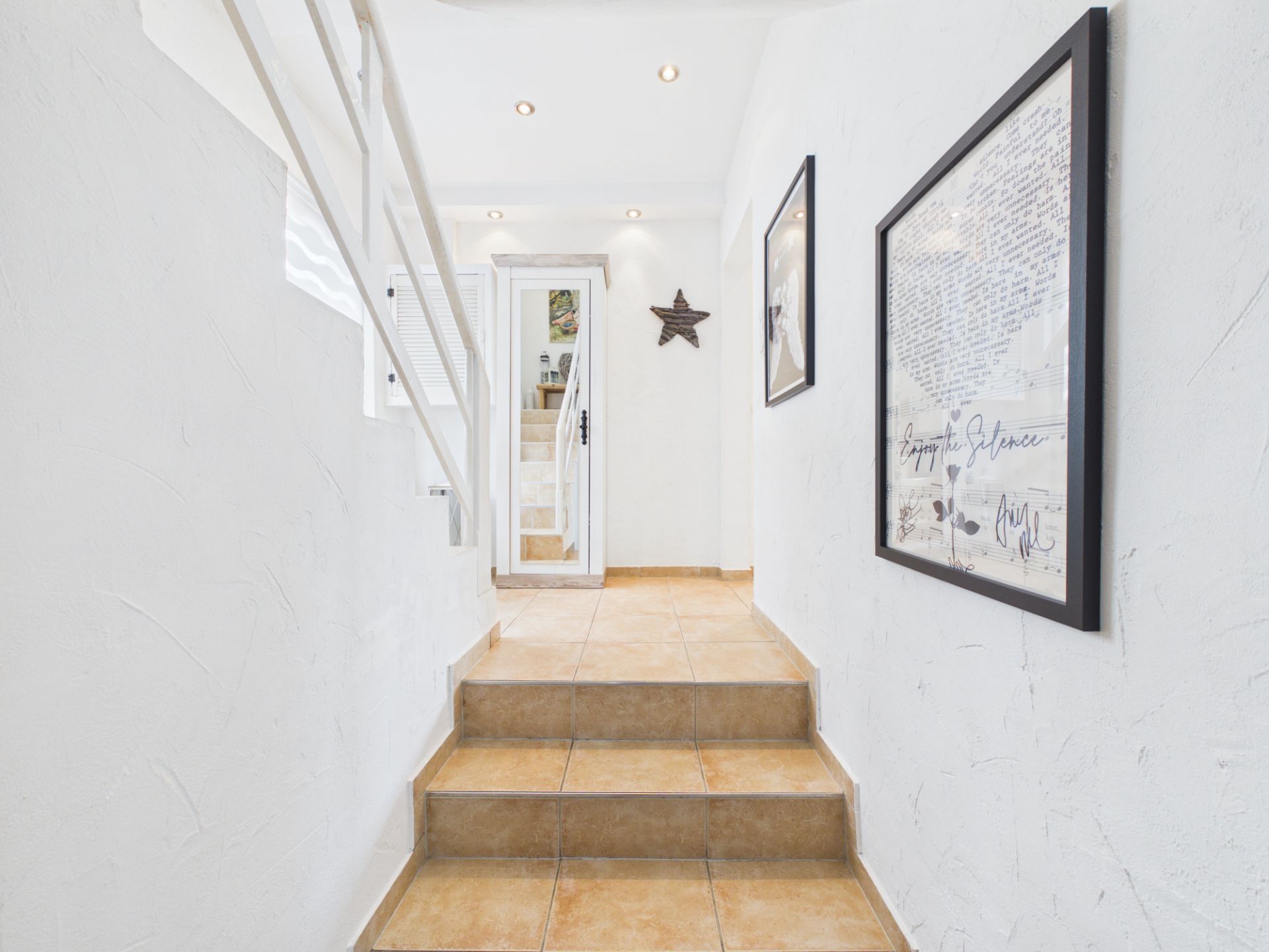 Heller Flur mit weißen Wänden, Bildern, Treppe und braunen Fliesen.