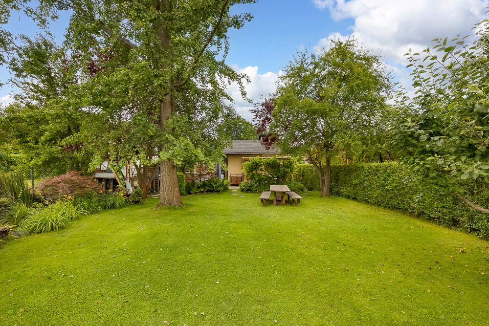 Grüner Garten mit Bäumen, einer Hecke und einem Holztisch mit Bänken auf dem Rasen.