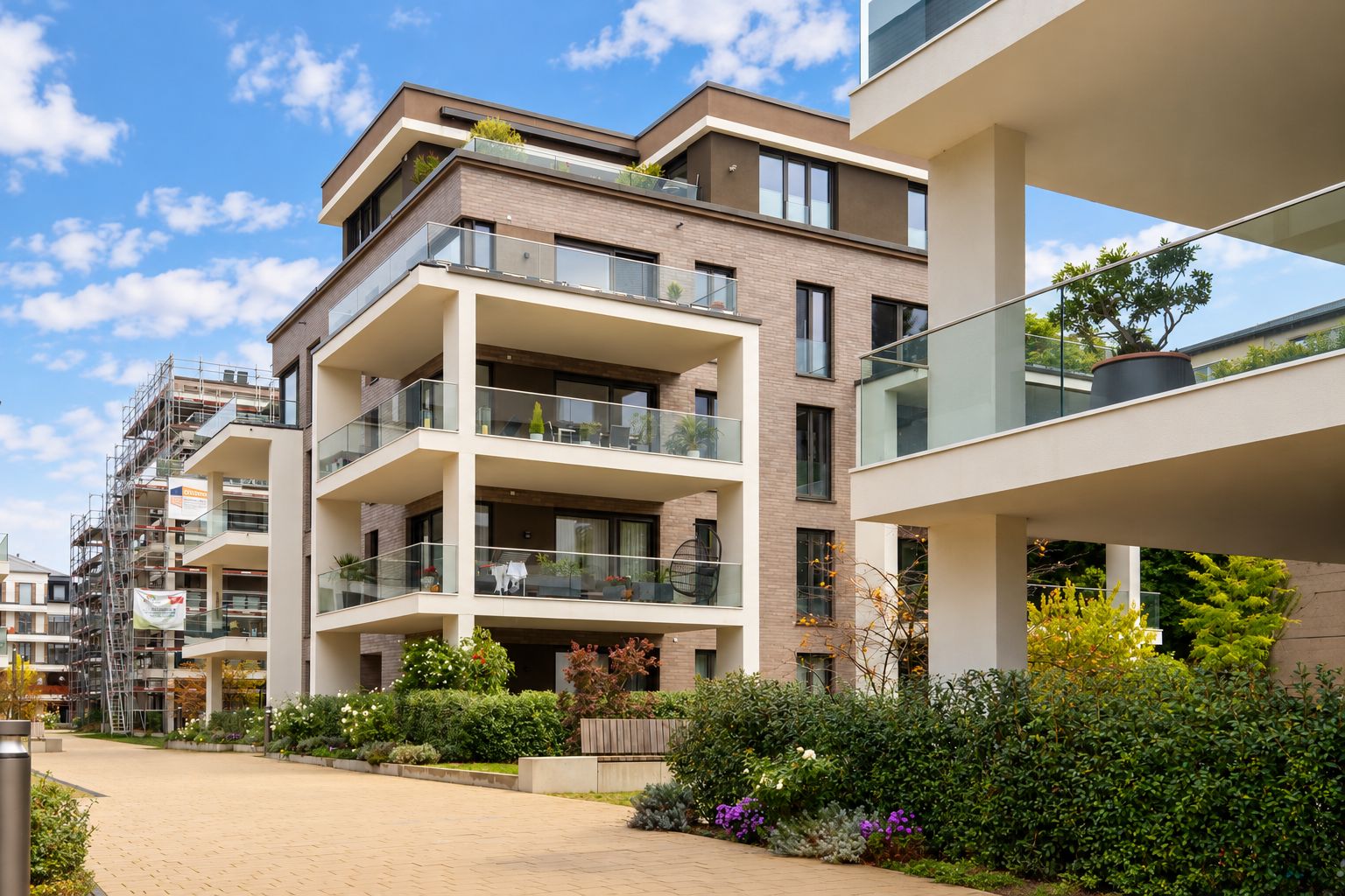 Modernes Wohnhaus mit mehreren Balkonen und Glasgeländern, umgeben von Grünanlagen.