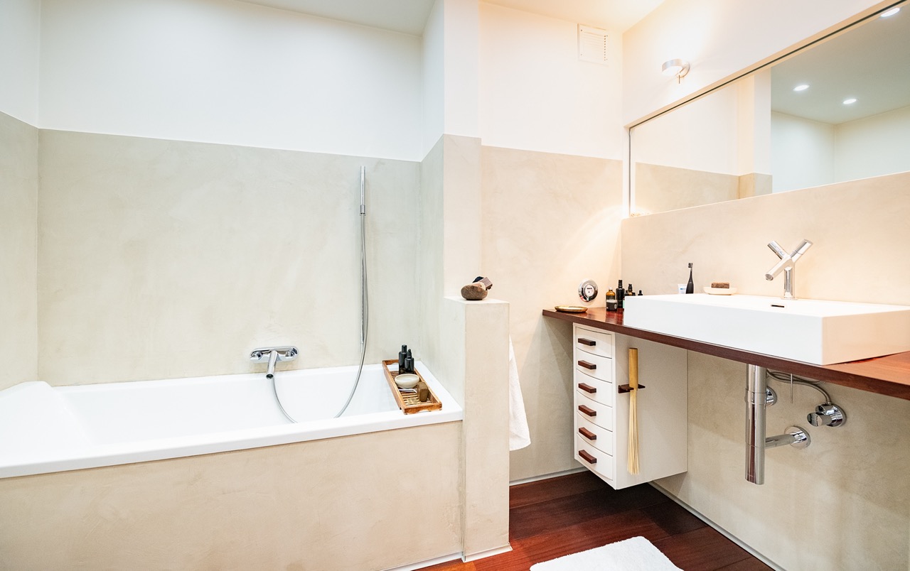 Modernes Badezimmer mit Badewanne, großem Waschbecken und Spiegel, hellen Wänden und Holzboden.