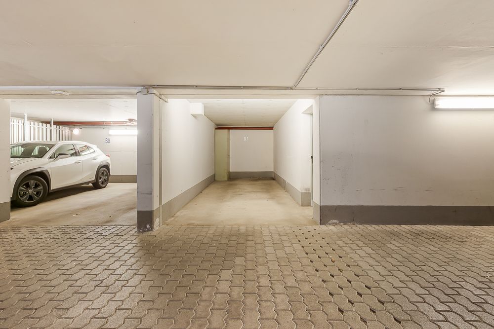 Leerer Tiefgaragenstellplatz neben einem geparkten weißen Auto in einer hell beleuchteten Garage.
