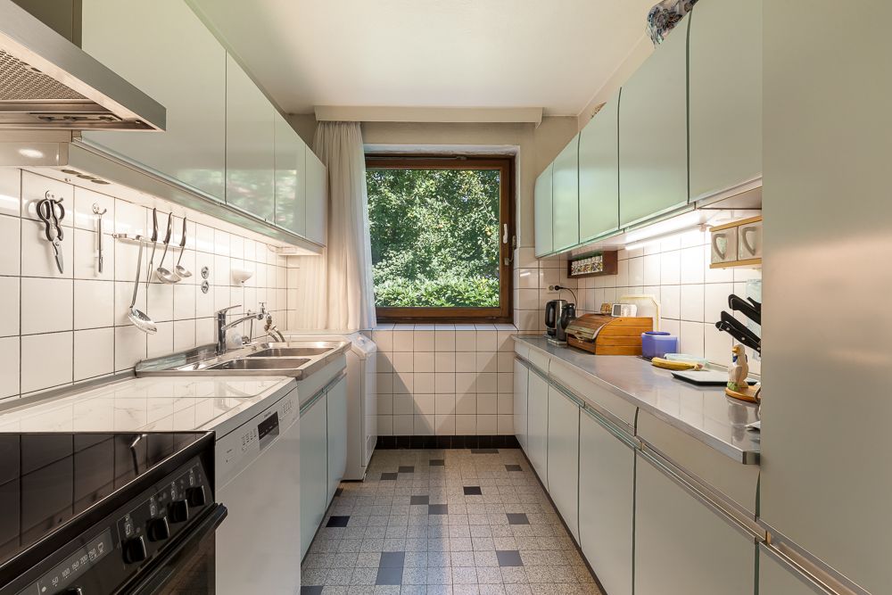 Helle, schmale Küche mit weißen Schränken, großem Fenster und Geräten.