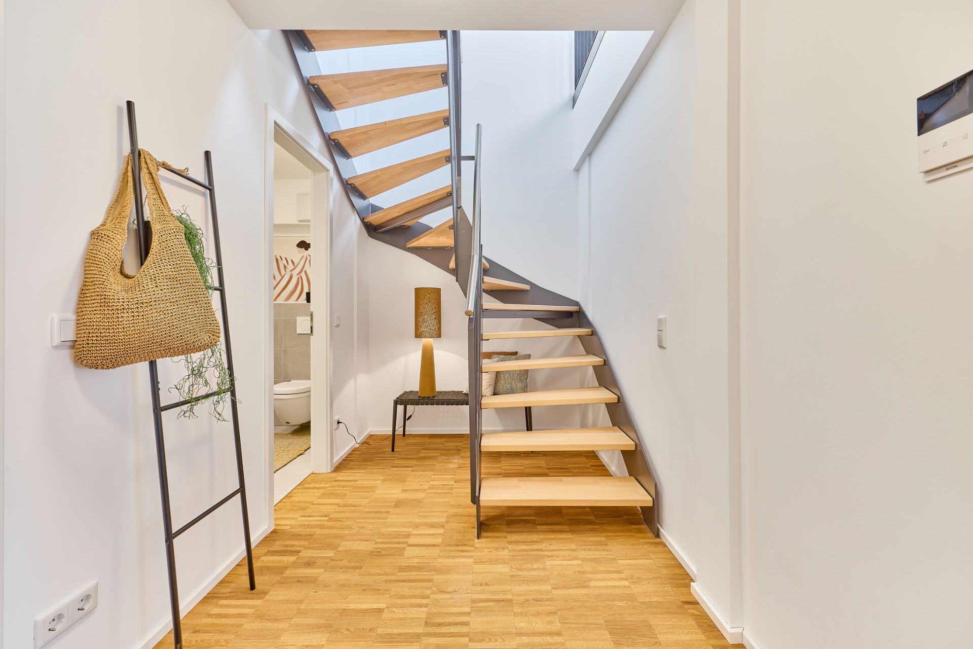 Moderner Flur mit Holztreppe, Holzfußboden und Zugang zu einem Badezimmer.