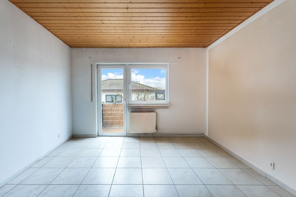 Leerer Raum mit Fliesenboden, Holzdecke, Fenster und Tür zum Balkon.